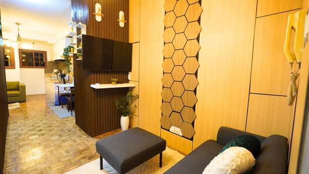 Een moderne woonkamer met een bank, een klein tafeltje, een televisie en een houten wand met honingraatpatroon.