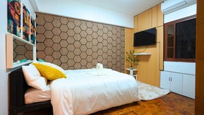 Een slaapkamer met een bed, een televisie, een houten wand met honingraatmotief en een raam.