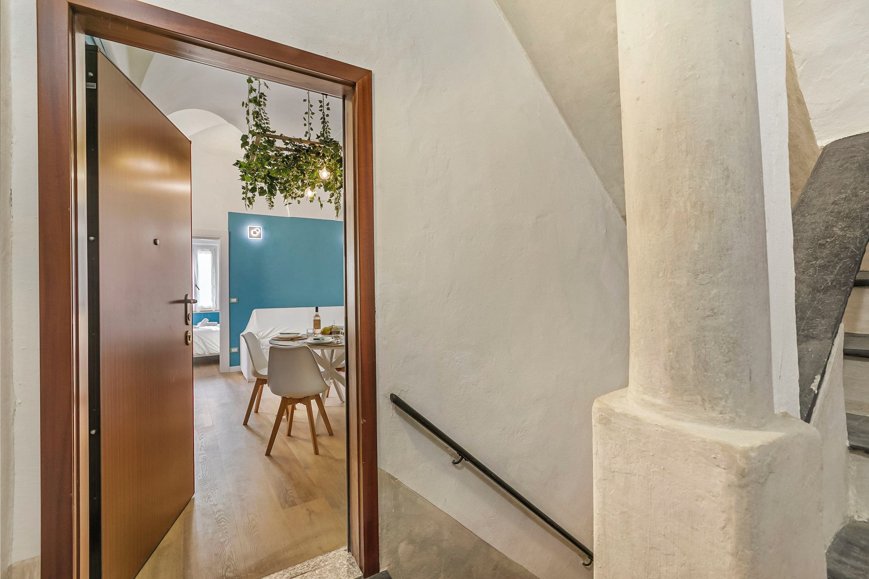 A staircase with a handrail, a wooden door, and a view into a dining area with chairs and a table.