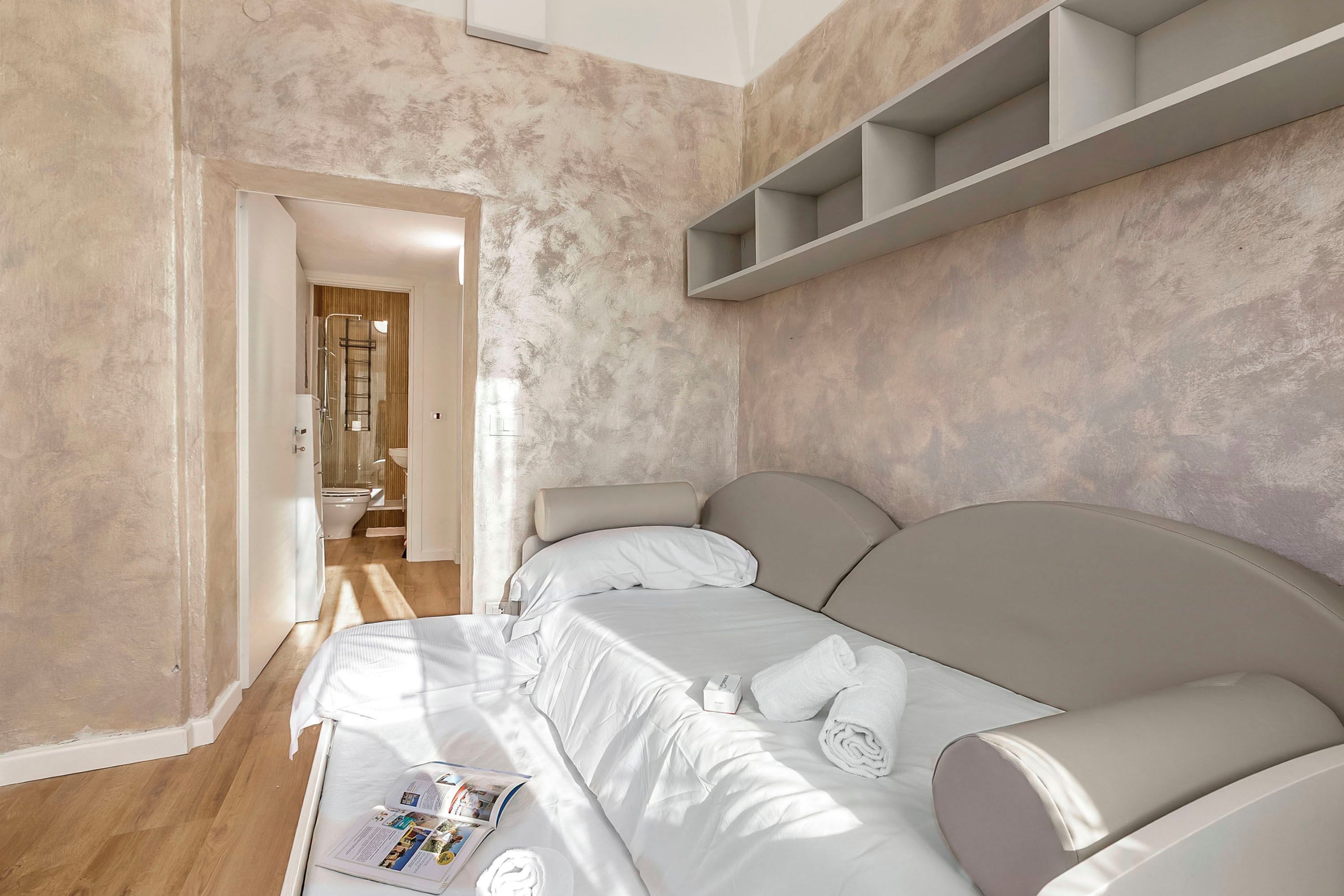 A bedroom with a bed, a bedside table, a towel, and a magazine.