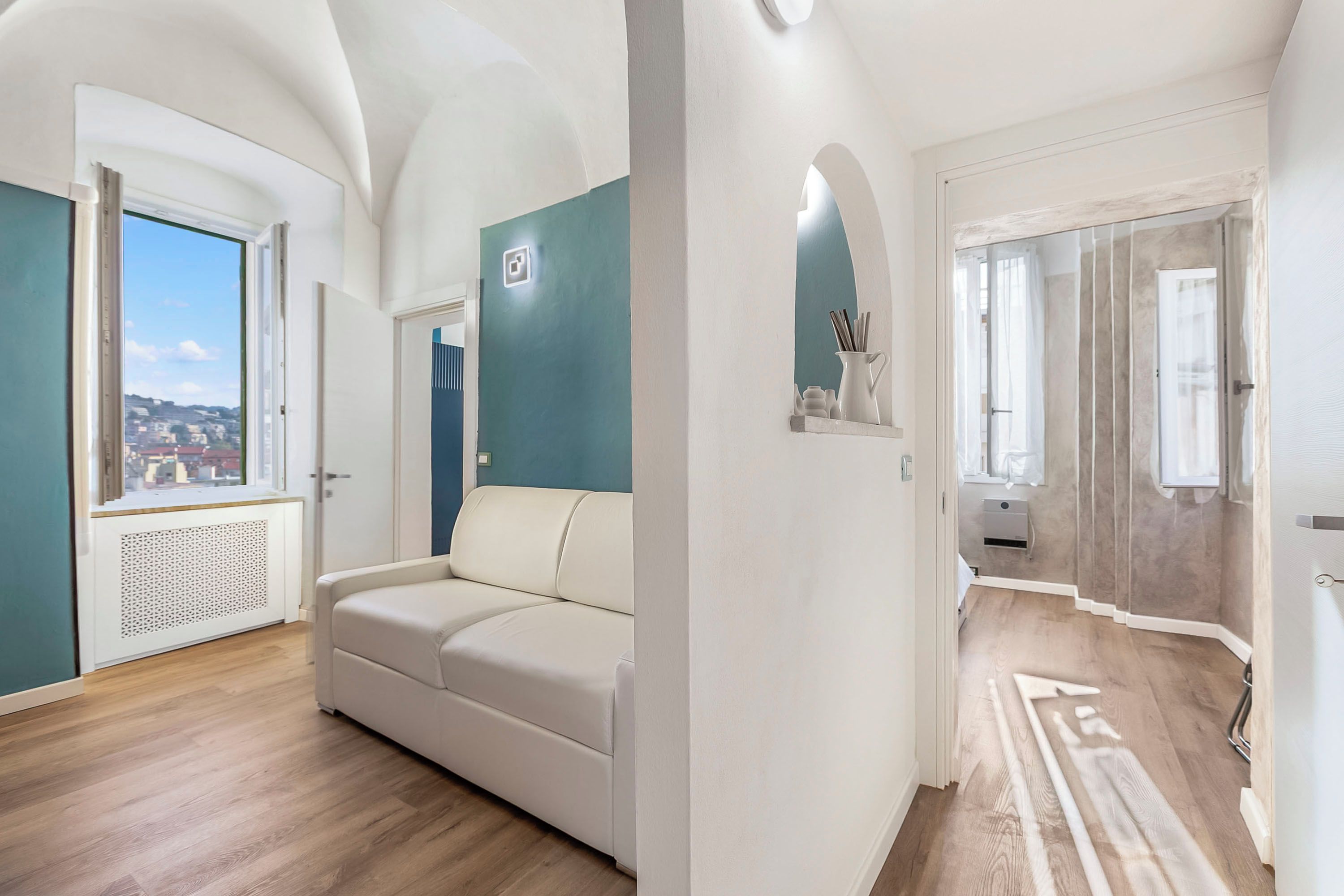 Ein Zimmer mit einem weißen Sofa, Blick durch ein Fenster, einer Tür und einem Spiegel.