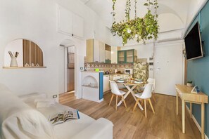 Una cocina moderna con armarios blancos, un comedor con sillas blancas y una planta colgante.