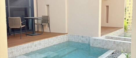 A swimming pool with a tiled deck, a ceiling fan, and a seating area with chairs and a table.