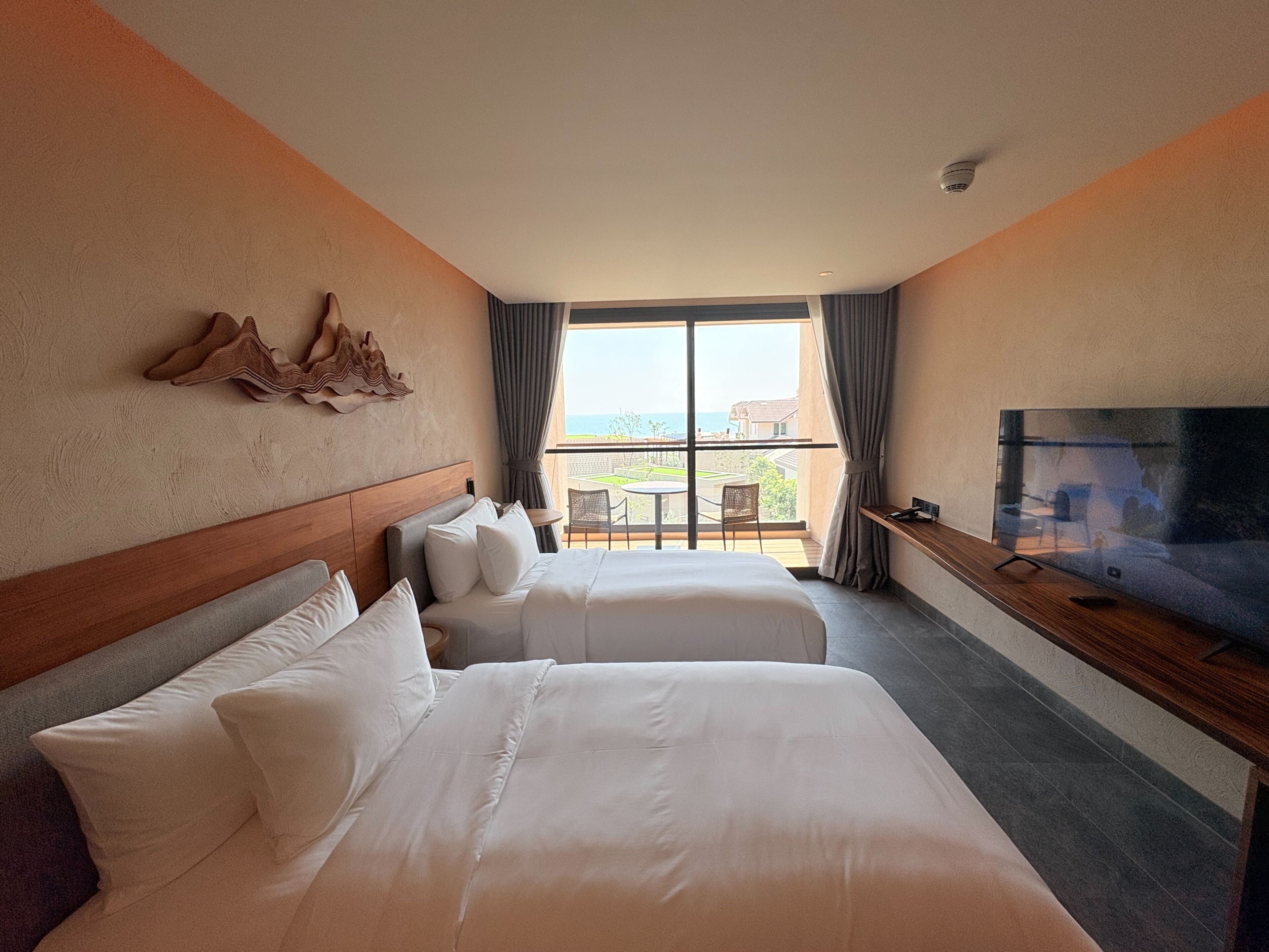 A hotel room with two beds, a TV, a balcony with a view, and a decorative wall piece.