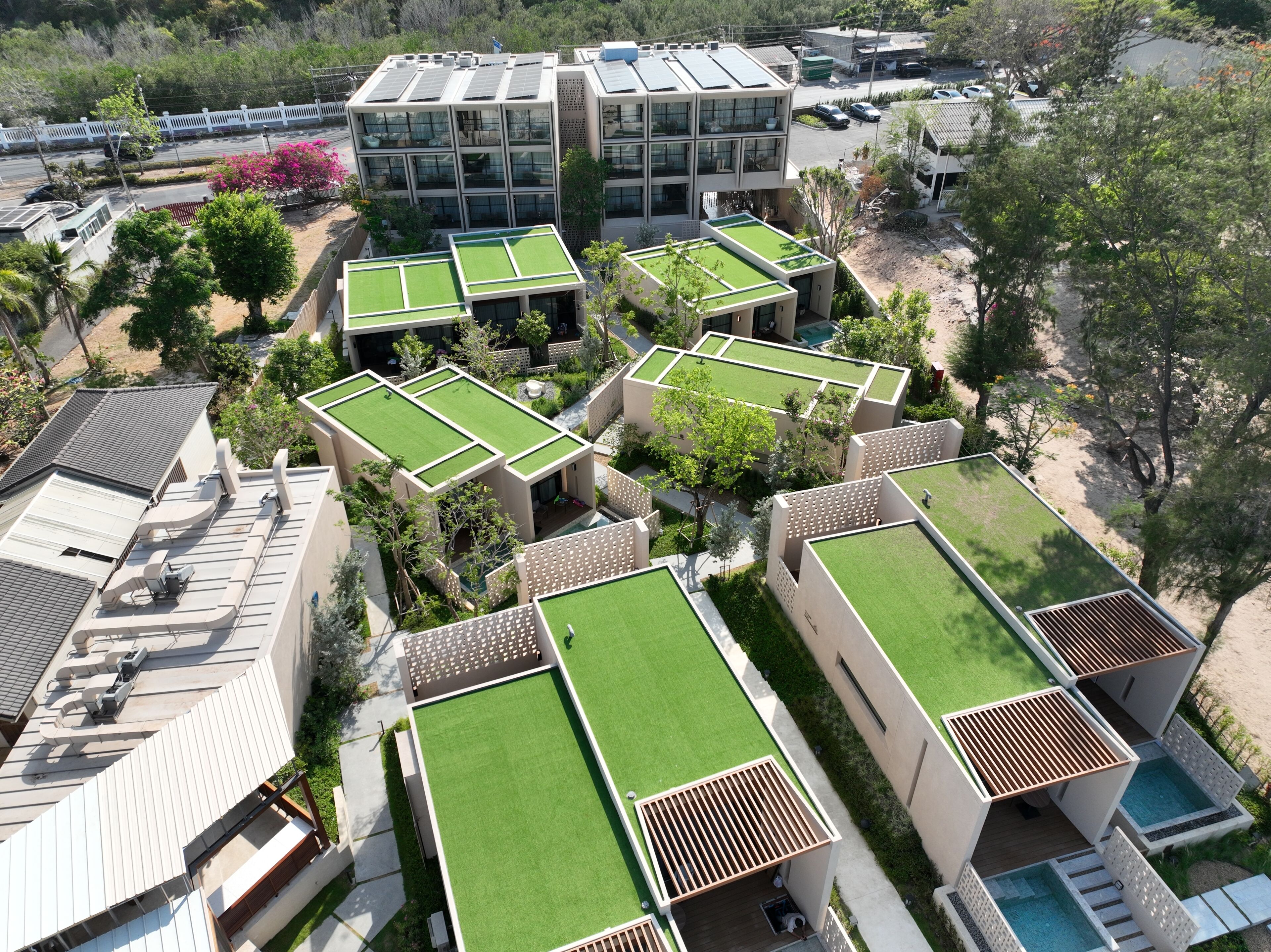 Un bâtiment moderne doté de nombreuses terrasses sur le toit, avec de l’herbe et des espaces aménagés autour de piscines.