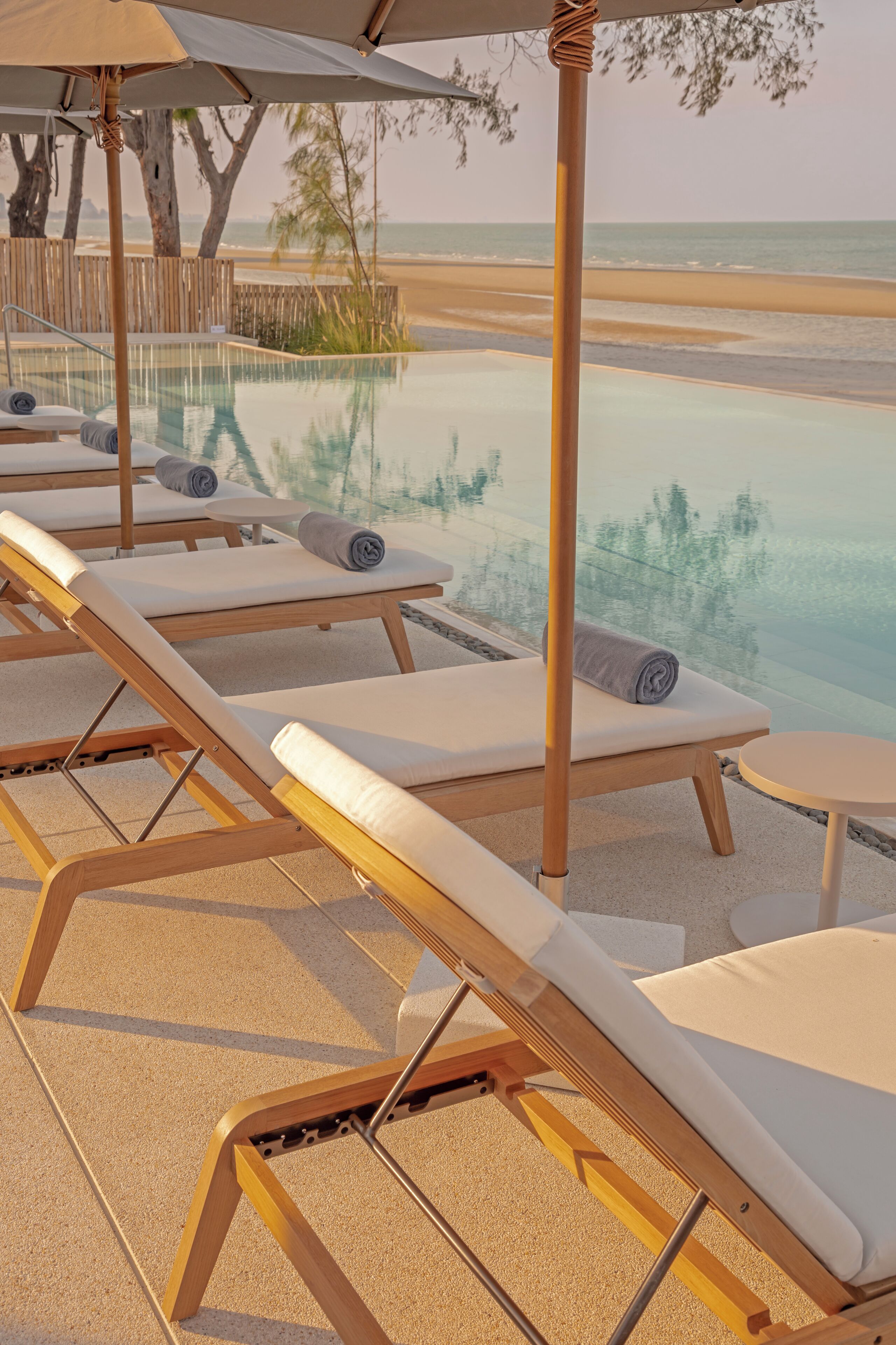 A poolside area with lounge chairs and a glass-bottomed infinity pool overlooking the beach.