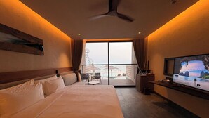 A hotel room with a large bed, a television, a balcony with a view of the sea, and a ceiling fan. - Riva Hua Hin (Hua Hin)