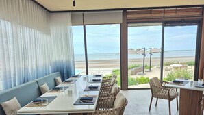 A dining area with a view of the beach, a sofa, and a table set for two. - Riva Hua Hin (Hua Hin)