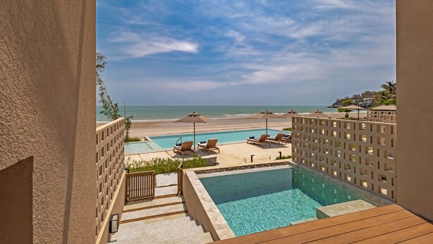 A pool area with lounge chairs and umbrellas, a view of the beach, and a clear sky. - Riva Hua Hin (Hua Hin)