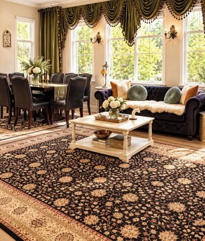 A room with a dining table set for four, a sofa with cushions, and a patterned rug.