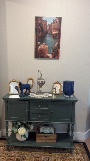 Een groene dressoir met decoratieve objecten, een ingelijste foto erboven en een kamerkleed eronder.