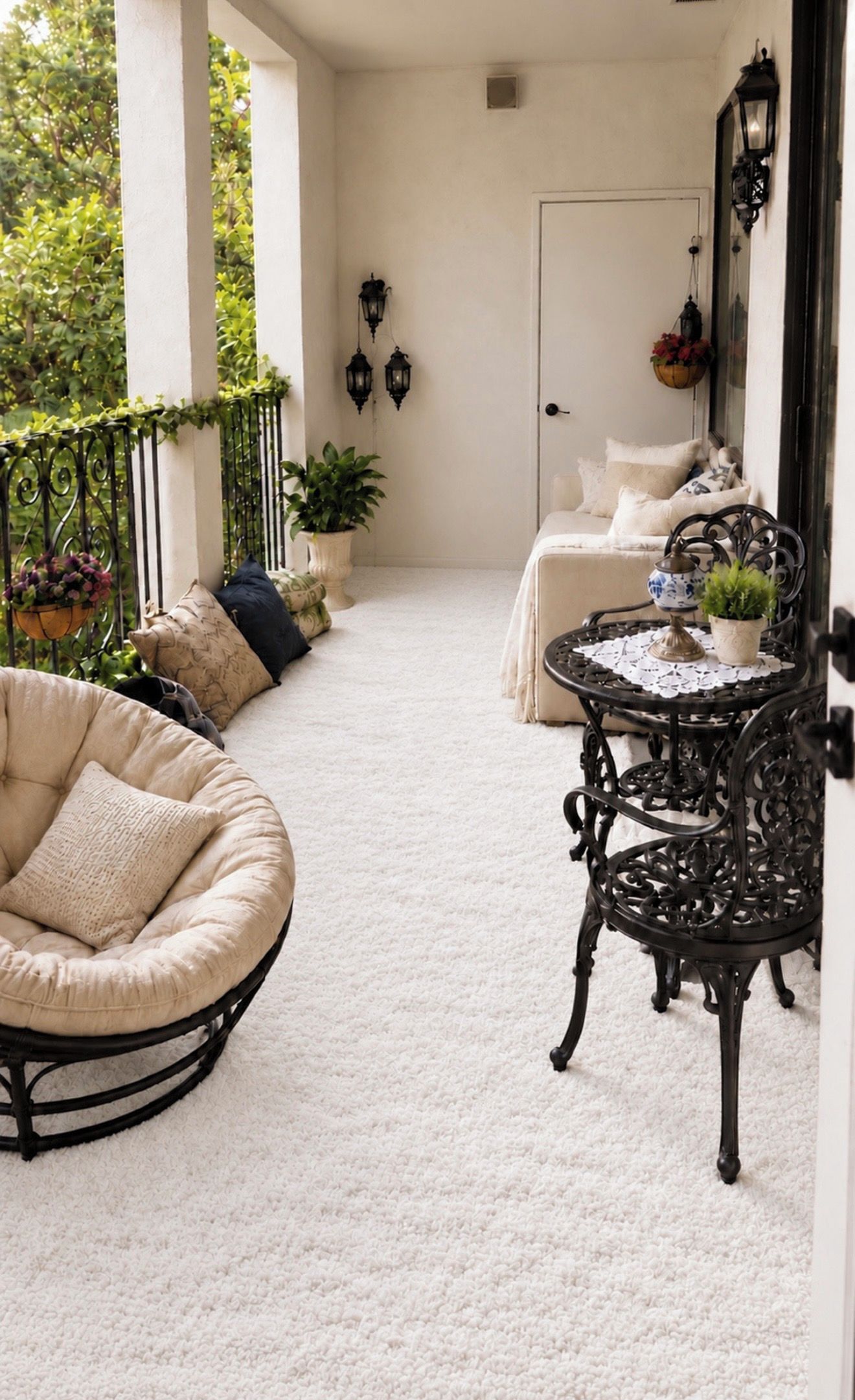 A cozy balcony with a white chair, a small table with a plant, and a sofa with cushions.