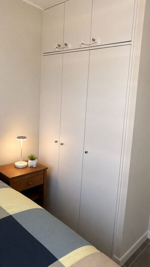 A bedroom with a bed, a bedside table with a lamp, and a wardrobe.