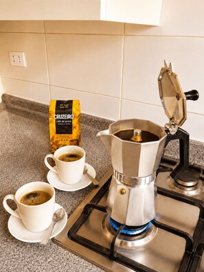A kitchen with a coffee maker, two cups of coffee, and a packet of coffee.