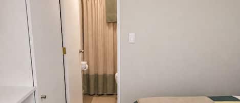 Un dormitorio con cama, armario, baño con cortina de ducha y una toalla sobre la cama.