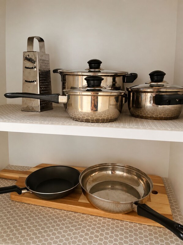 A kitchen with stainless steel cookware on a white shelf and a wooden cutting board with a frying pan and a strainer.