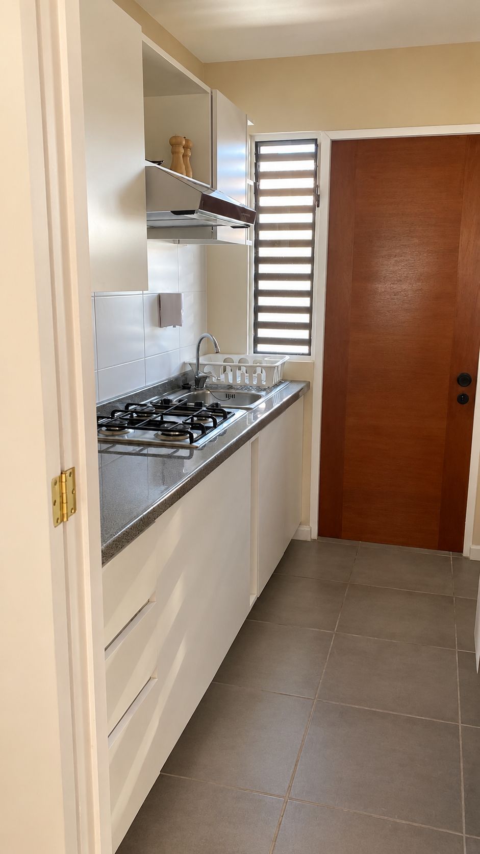 Une cuisine équipée d’une cuisinière à gaz, de meubles blancs et d’une fenêtre avec des stores.