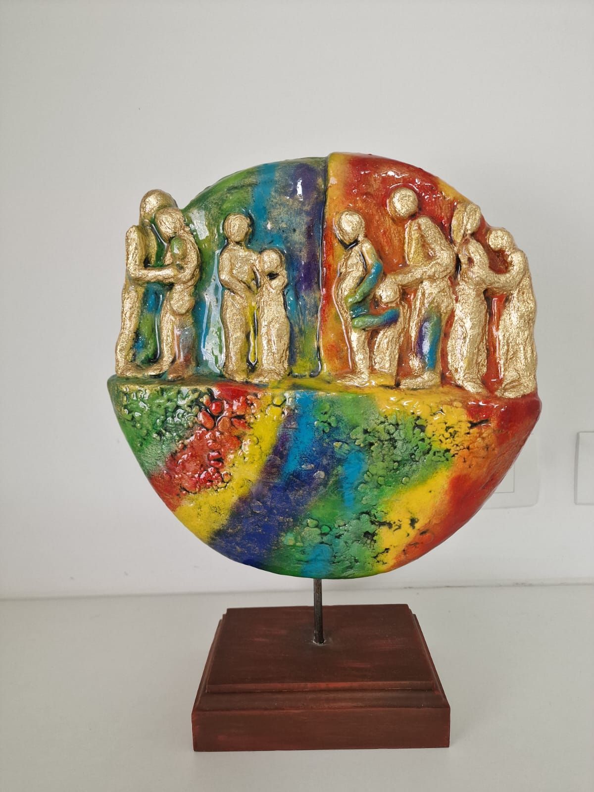 A colorful sculpture with figures on a wooden base.