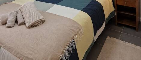 A neatly made bed with a checkered bedspread, a wooden headboard, and a bedside table with a lamp.