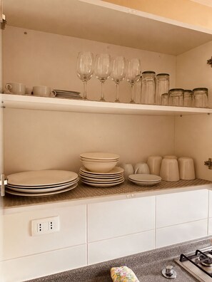 Una cocina con armarios blancos, una encimera con vasos, platos y frascos.