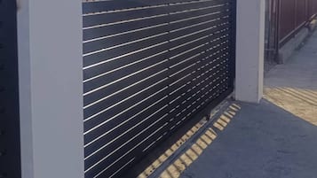 Una reja de metal negro con listones horizontales, pilares blancos y suelo empedrado.