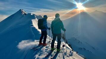 Two skiers on a snowy mountain peak with a sunrise in the background.