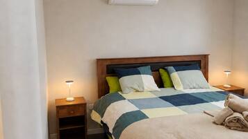 A bedroom with a bed, bedside tables, a wall-mounted air conditioner, and a ceiling light fixture.