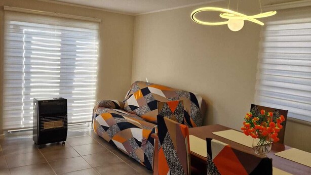 Un salon comprenant un canapé, une table à manger avec des chaises, un radiateur et un luminaire fixé au plafond.