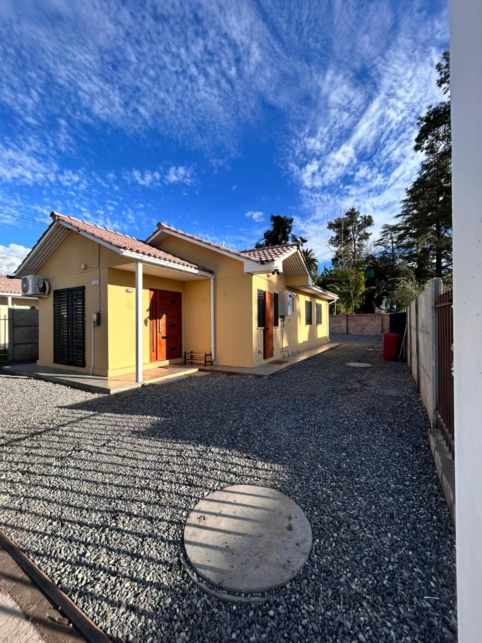 Um edifício residencial com telhado de cerâmica, entrada por um caminho de cascalho e tampa de metal para bueiro.
