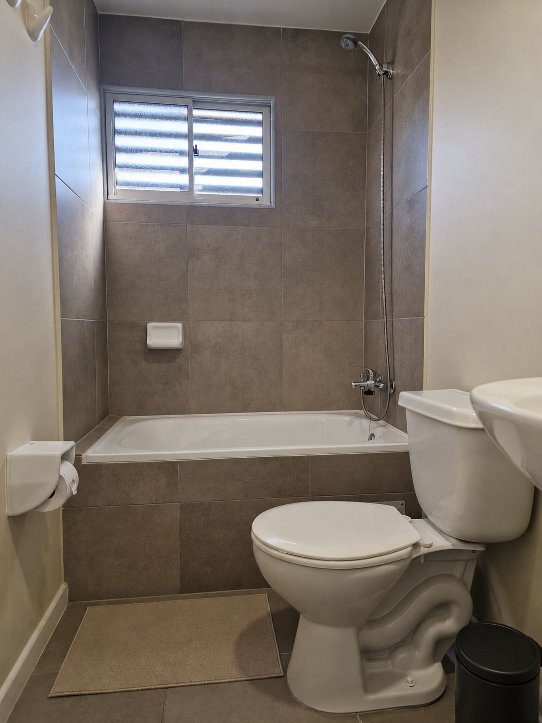 Ein Badezimmer mit Badewanne, Toilette und einem Fenster mit Jalousien.