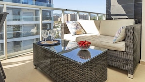 Een balkon met een rieten bank, een glazen bijzettafeltje met een schaal fruit, en twee wijnglazen.