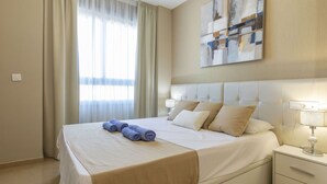 Een hotelkamer met een groot bed, een nachtkastje, een lamp, een schilderij aan de muur en een raam met gordijnen.