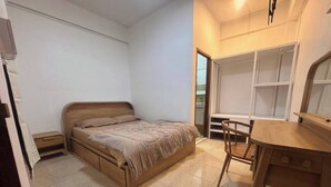 Een slaapkamer met een bed, een bureau en een stoel. Er is een kledingkast en een deur naar een andere kamer.
