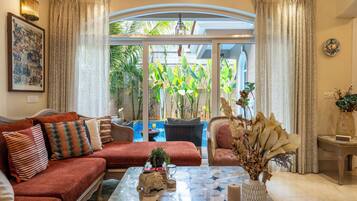 A living room with a sofa, armchairs, a coffee table, and a view of a pool and greenery outside.