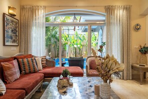 A living room with a sofa, armchairs, a coffee table, and a view of a pool and greenery outside. - Staymaster Una 4BR Villa (Assagao)