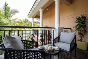 A balcony with wicker furniture, a potted plant, and a view of a red-roofed building. - Staymaster Una 4BR Villa (Assagao)