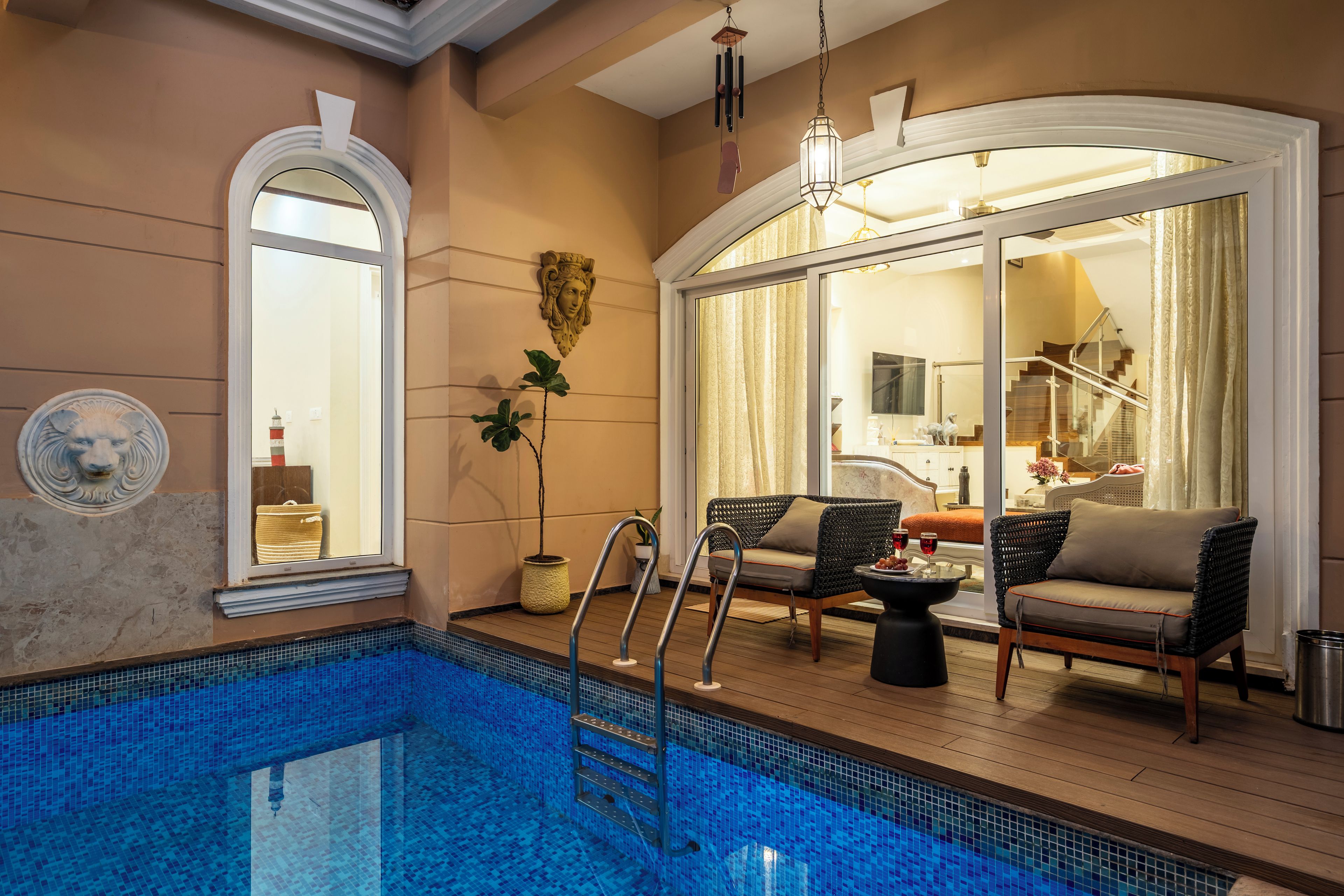 A pool area with a wooden deck, lounge chairs, and a glass-enclosed room with a view.