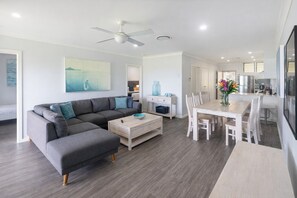 Ein modernes Wohnzimmer mit einem grauen Ecksofa, einem Holztisch und einem Essbereich mit weißem Tisch und Stühlen.