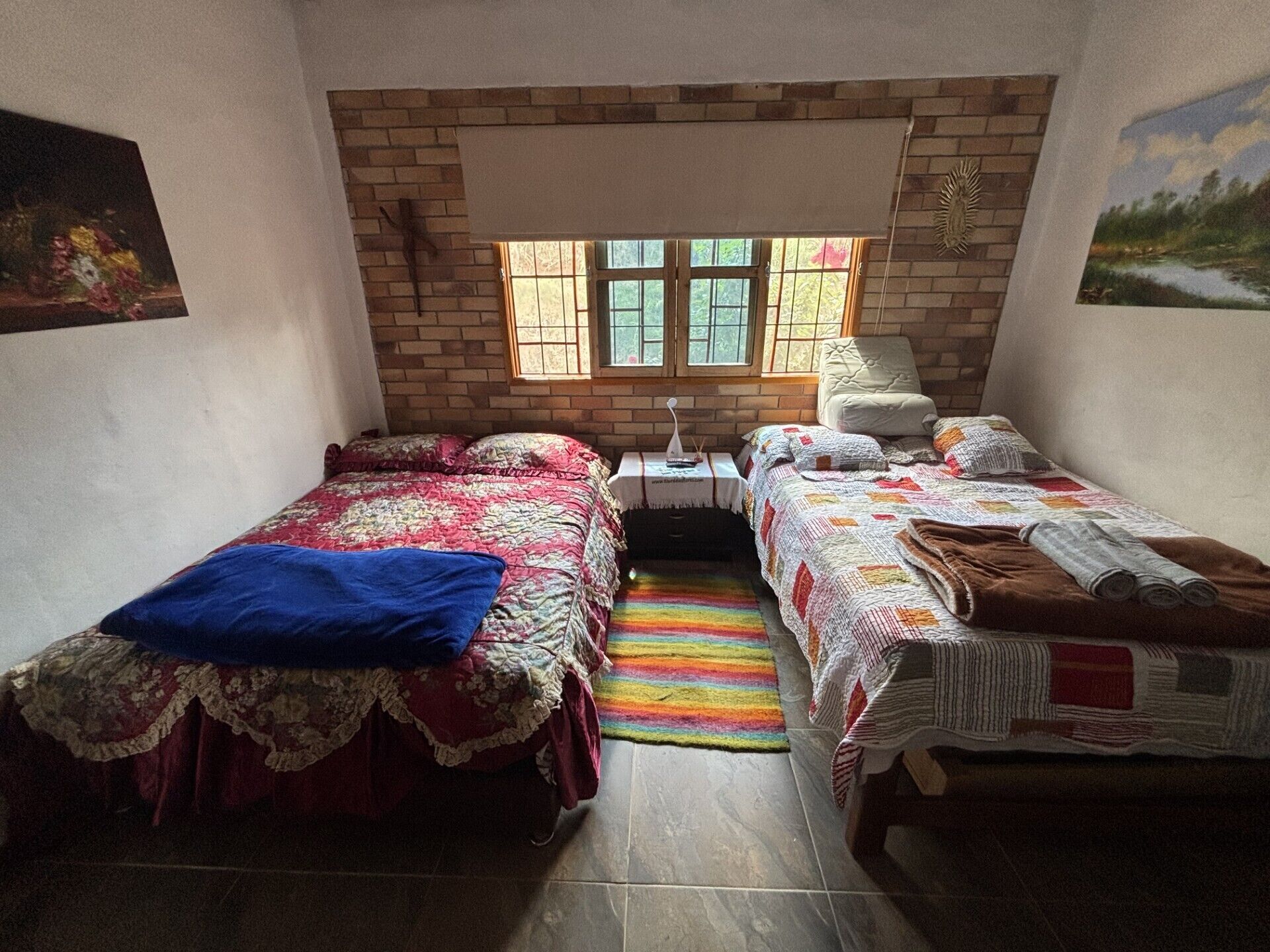 A bedroom with two beds, a window, a chair, and a small table.