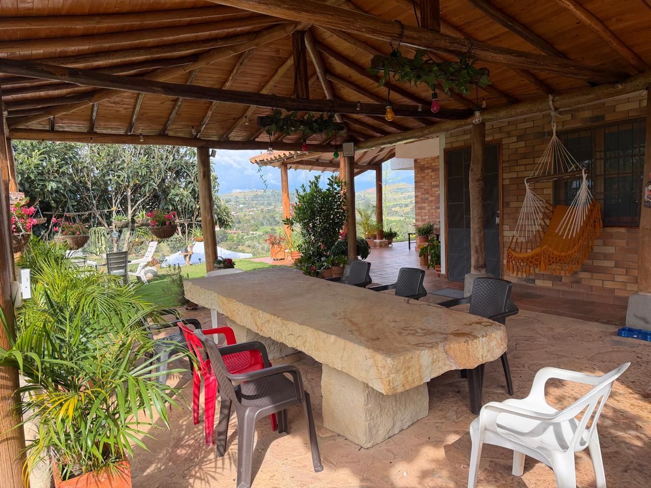 Un patio al aire libre con una mesa y sillas de piedra, rodeado de plantas en macetas y un muro de ladrillo.