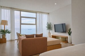 Ein modernes Hotelzimmer mit großem Fenster, Flachbildfernseher, Sofa, Bett und zwei Blumentöpfen.