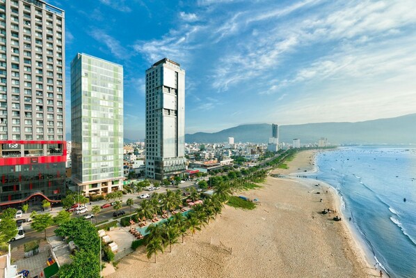 A coastal cityscape with modern high-rise buildings, a sandy beach, and a clear blue sky.