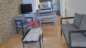 A living room with a television, a sofa, a bench, and a table with a vase of flowers. - Cozy apartment in quiet area with fantastic sea view and swimming pool, (Riviere Noire)