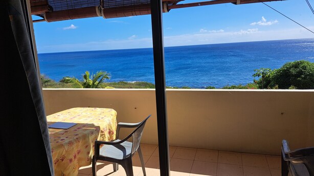 A balcony with a table and chairs, overlooking a coastal view. - Cozy apartment in quiet area with fantastic sea view and swimming pool, (Riviere Noire)
