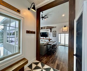 A modern interior with a wooden bench, a kitchen area with a dining table and chairs, and a large window overlooking a deck. - TT CastIron Open layout, EV, close2Yellowstone, hotTub, AC (Island Park)