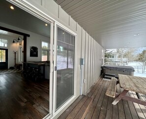 A covered porch with a wooden deck, a sliding glass door, and a view of a snowy landscape. - TTM Open layout, EV, close2Yellowstone, hotTub, AC (Island Park)