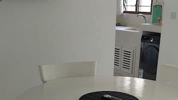 Una mesa redonda blanca con sillas acolchadas en azul, un mantel individual negro y un televisor montado en la pared.