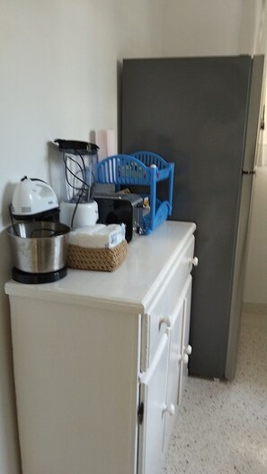 Una cocina americana con encimera blanca, refrigerador negro, una silla azul y varios electrodomésticos.