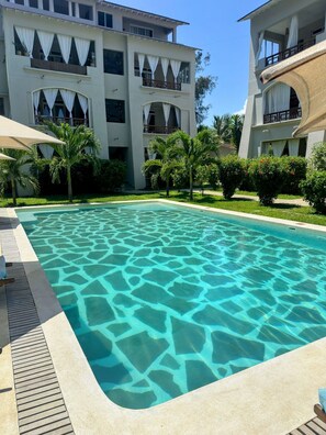 A swimming pool with clear water, surrounded by palm trees and a building with balconies. - Casa Di Philo 1
Four Steps To The Beach, (Watamu)