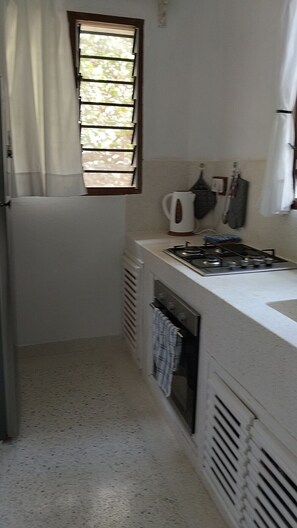 A compact kitchen with a gas stove, a kettle, and a window with blinds. - Casa Di Philo 1
Four Steps To The Beach, (Watamu)